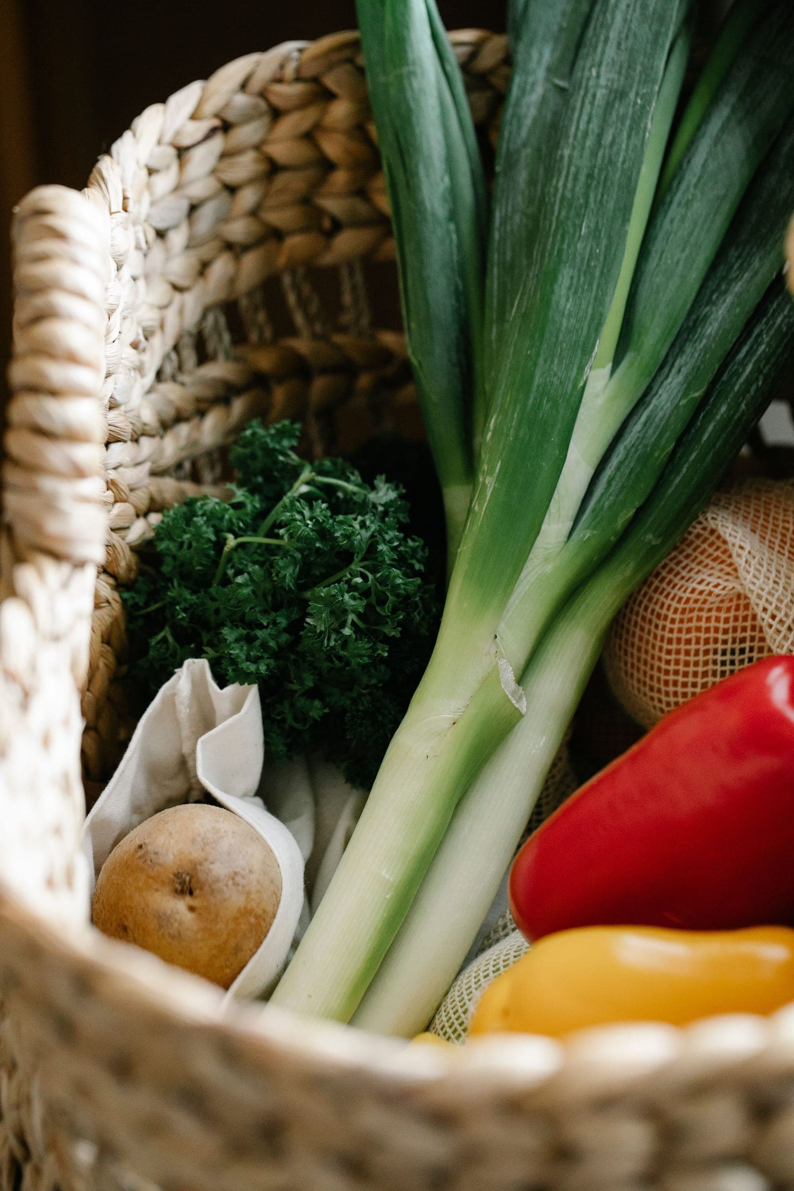 Cesta com legumes frescos: alho-poró, pimentões, batata e salsinha.